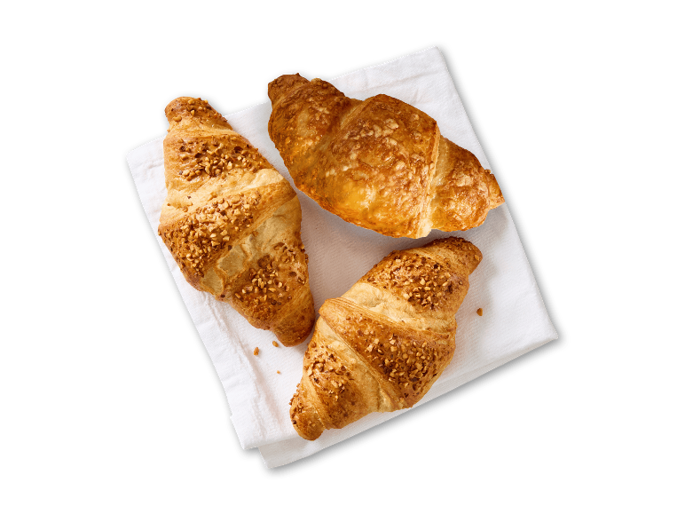 Tre croissanter, to af dem med nøddekrummer, på et hvidt klæde.