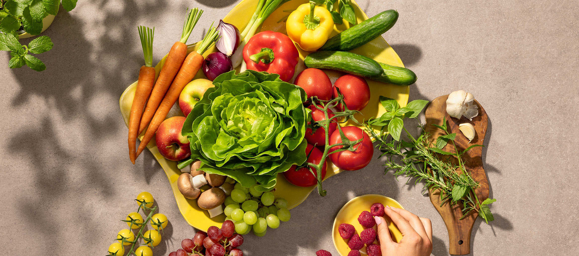 Friske grøntsager og frugter på et gult fad, herunder salat, tomater, gulerødder og bær.