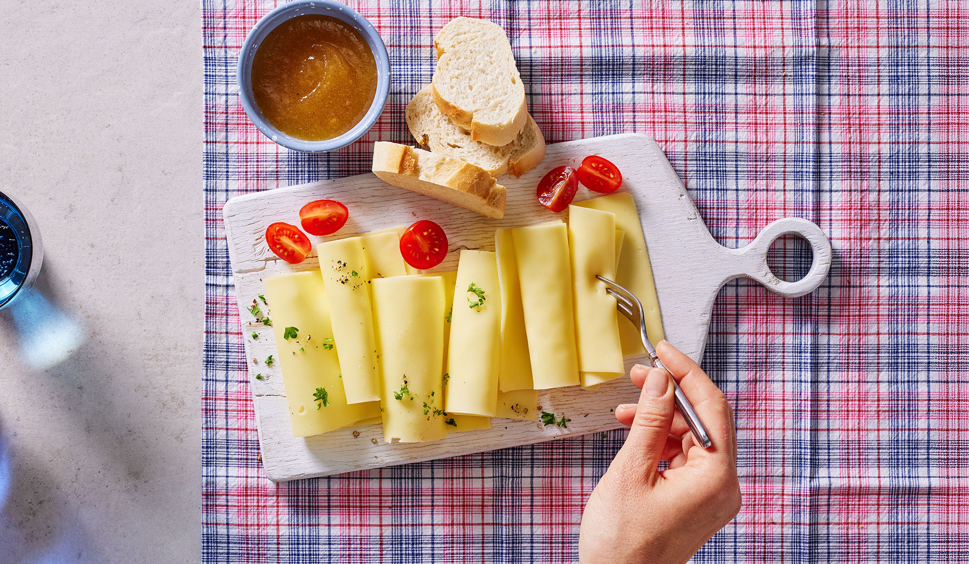 Osteskiver, cherrytomater, brød og syltetøj på et serveringsbræt.