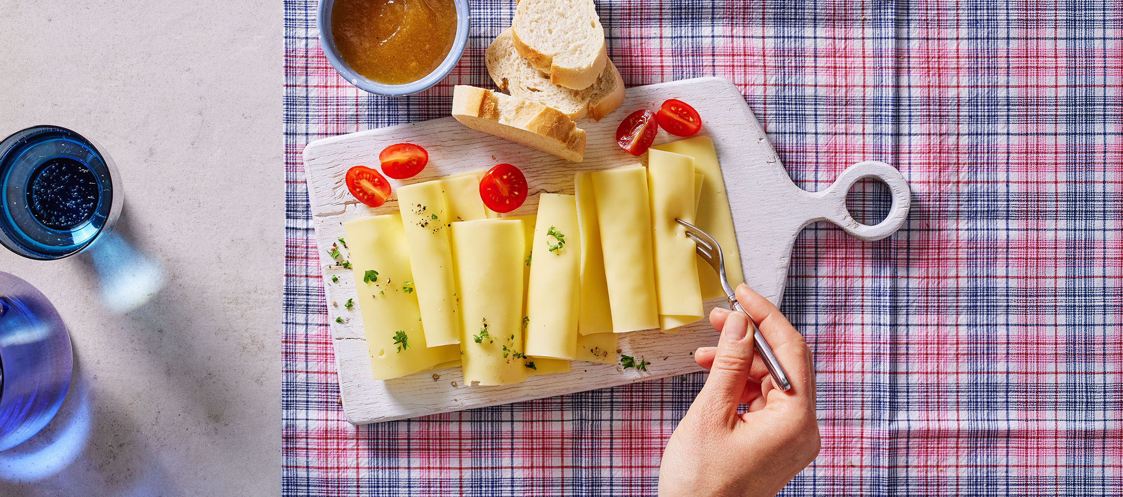 Osteskiver med cherrytomater, brød og marmelade på en ternet dug.