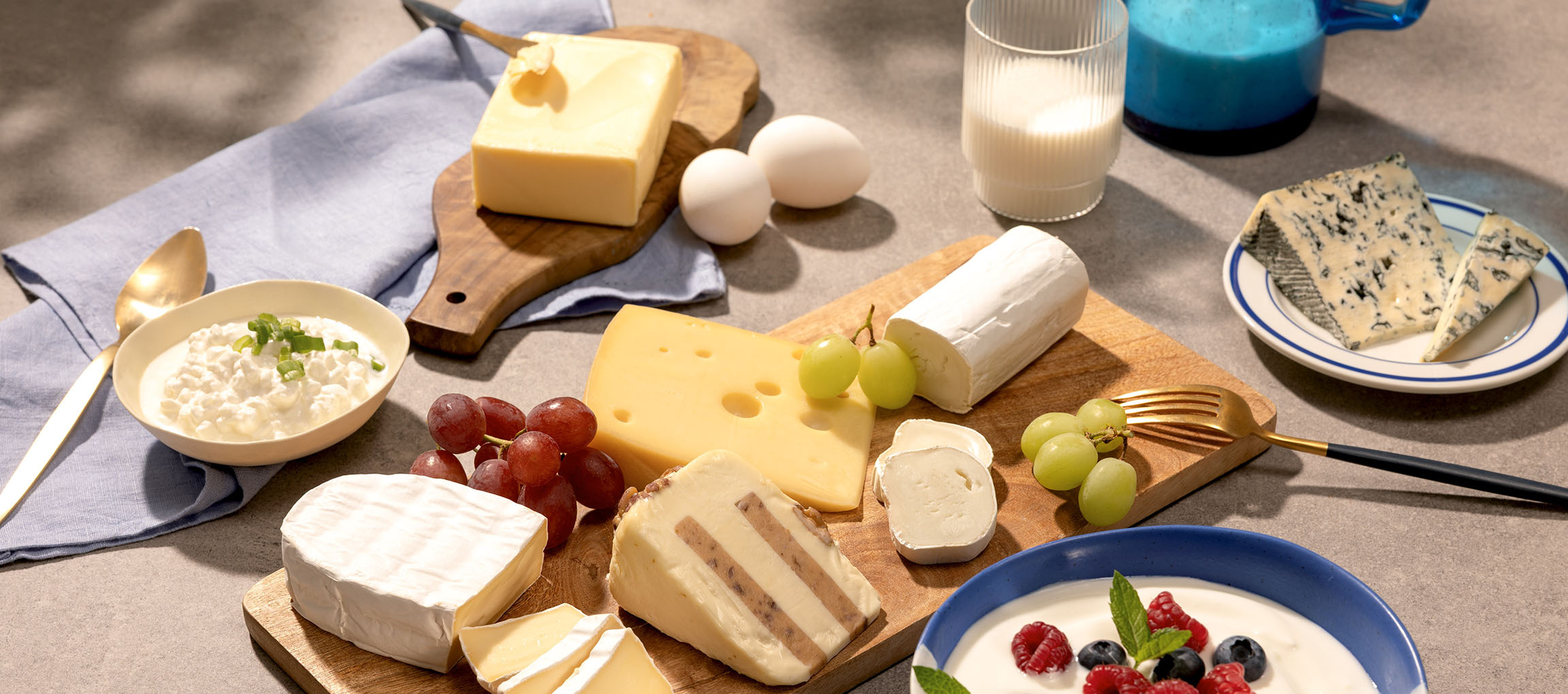 Diverse oste, æg, druer, mælk og yoghurt med bær på et bord.
