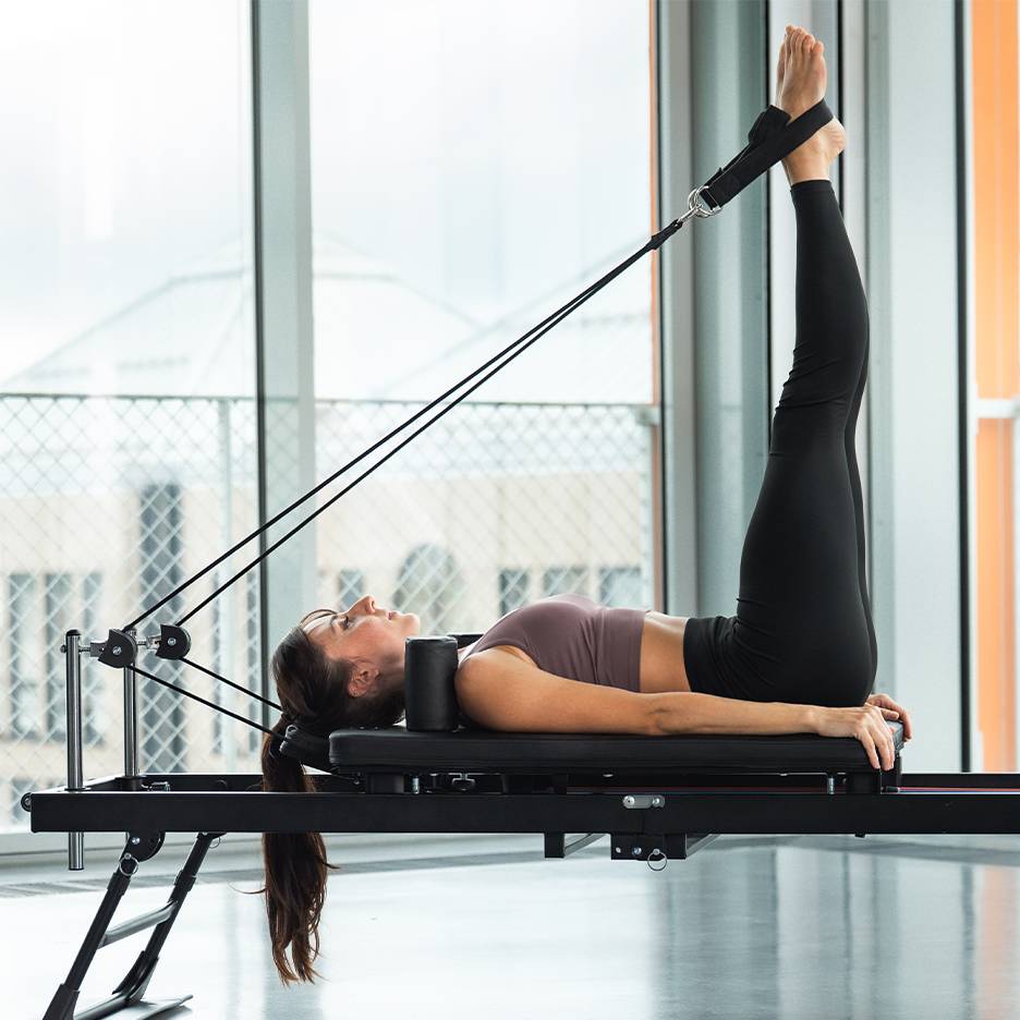 Kvinde laver benøvelse på en pilates reformer maskine.