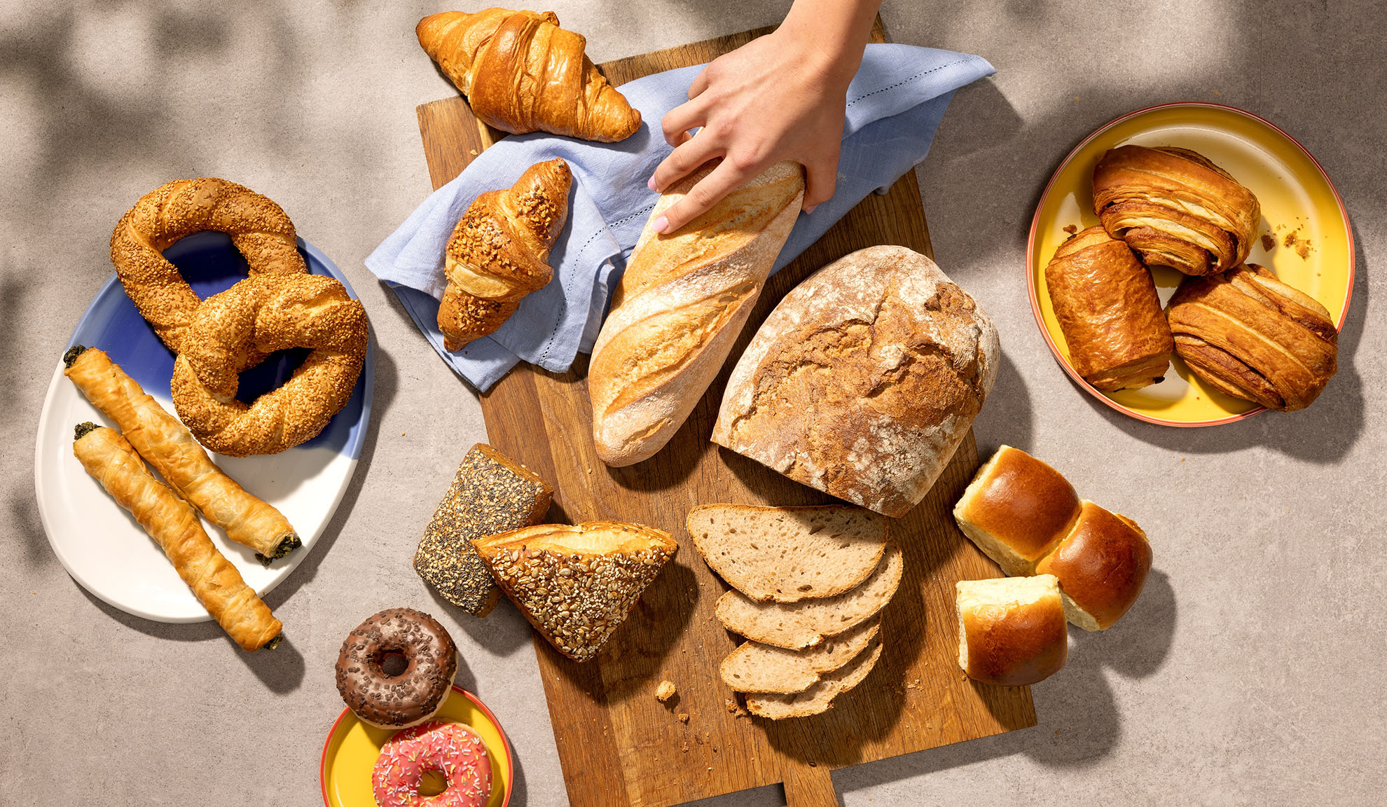 Udvalg af friskbagte varer, herunder brød, croissanter, kager og donuts på et bord.