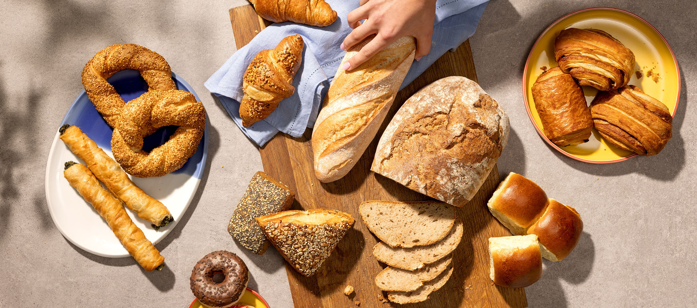 Udvalg af bagværk og brød, herunder kringler, croissanter og baguetter, på et bord.