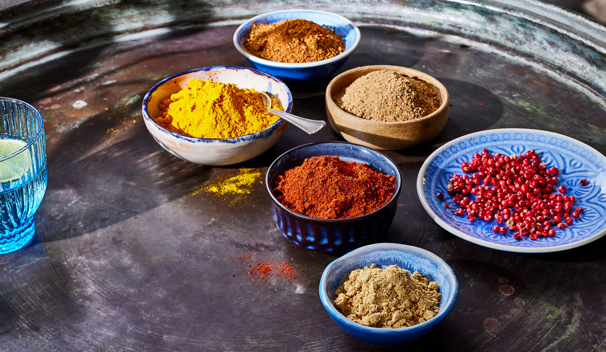 Forskellige krydderier i skåle: gurkemeje, paprika, peber og andre på en metalbakke.