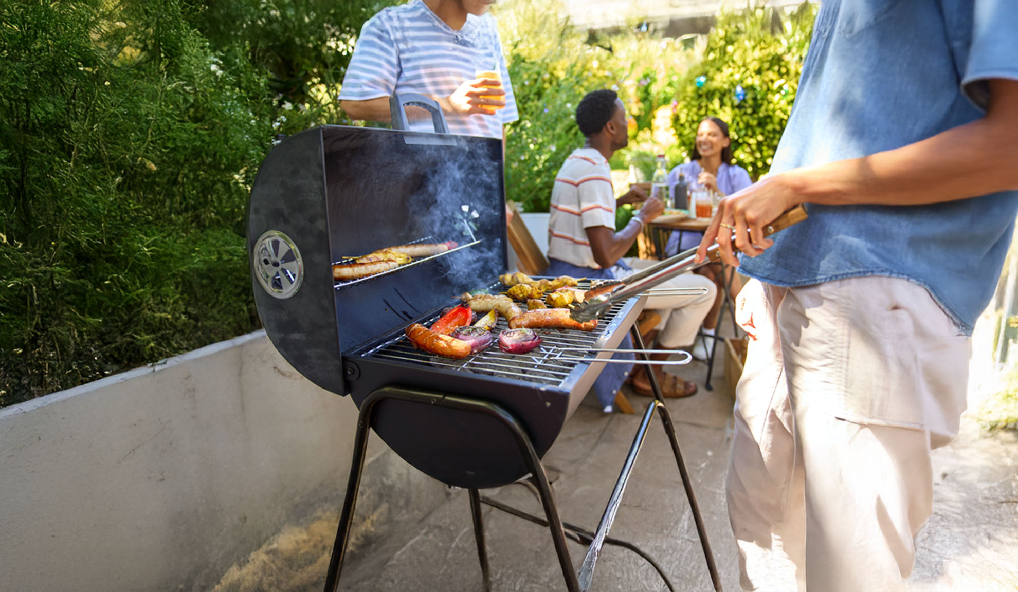 Venner nyder en grillfest med pølser og grøntsager i haven.