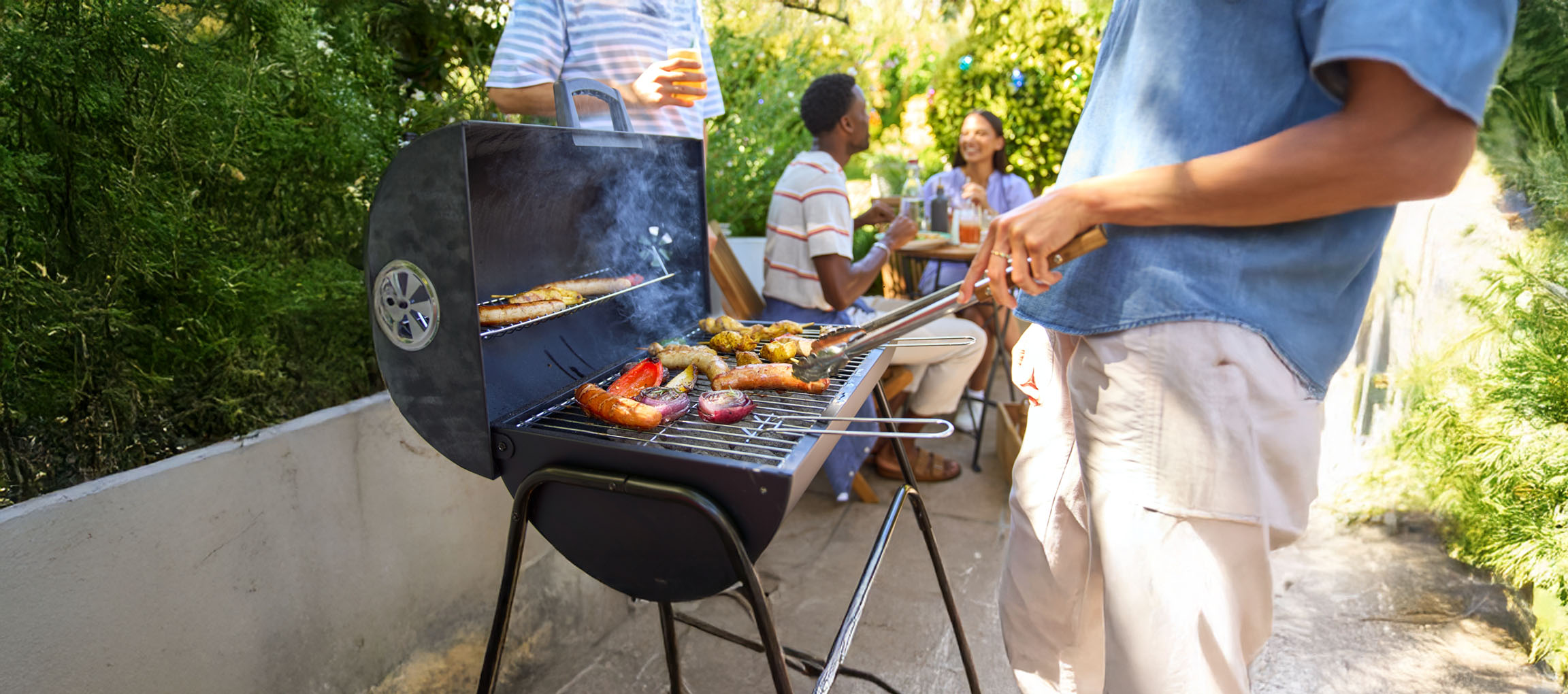 En kulgrill med grillede pølser og grøntsager.