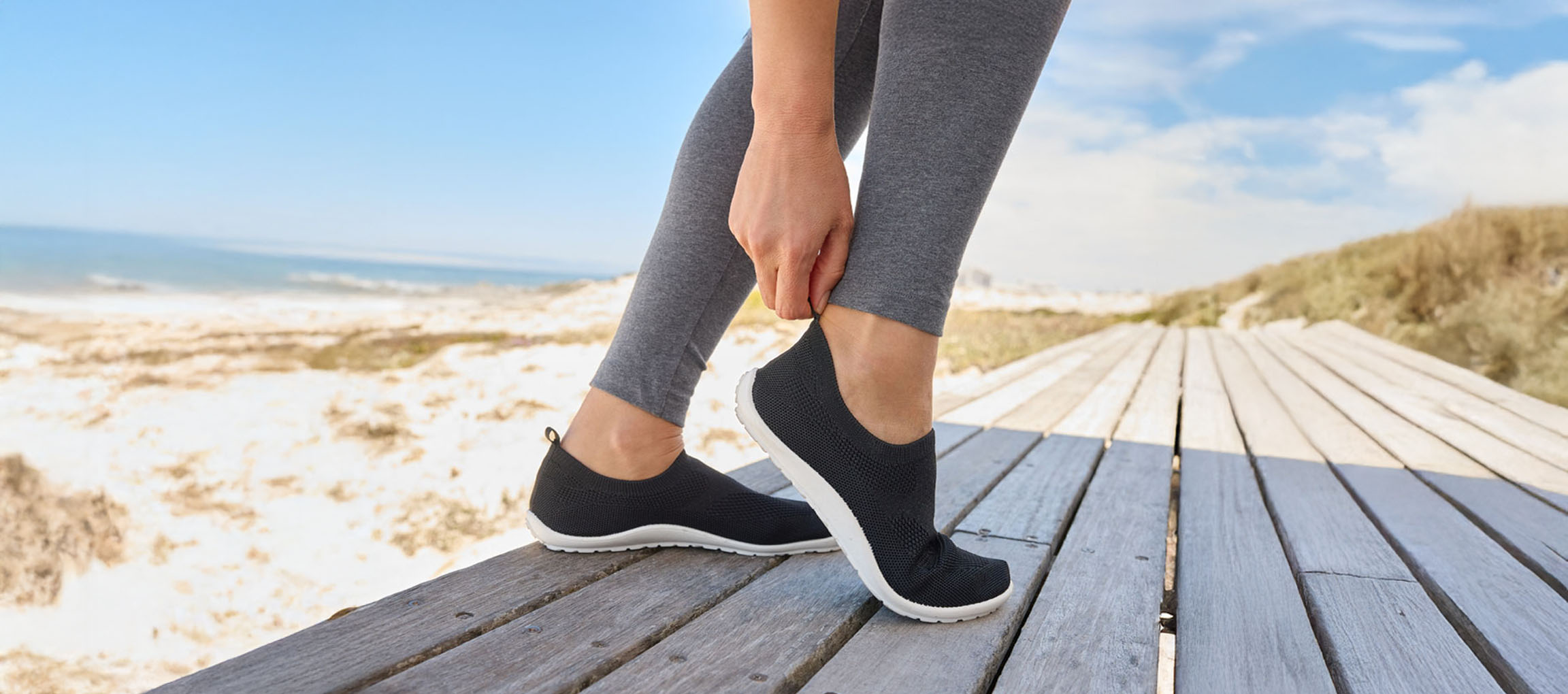 Kvinde tager sorte sneakers på ved stranden.