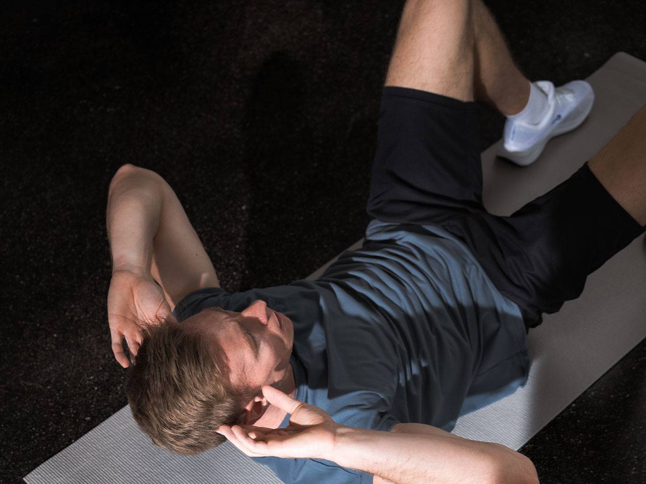 Mand i blå T-shirt og sorte shorts laver mavebøjninger på en yogamåtte.