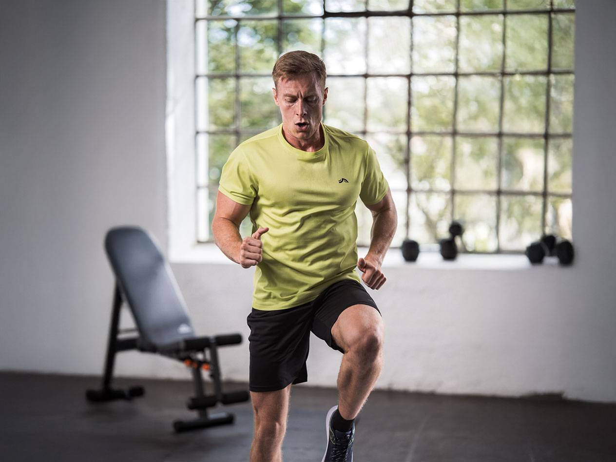 Mand i gul T-shirt og sorte shorts løber i et fitnesscenter.