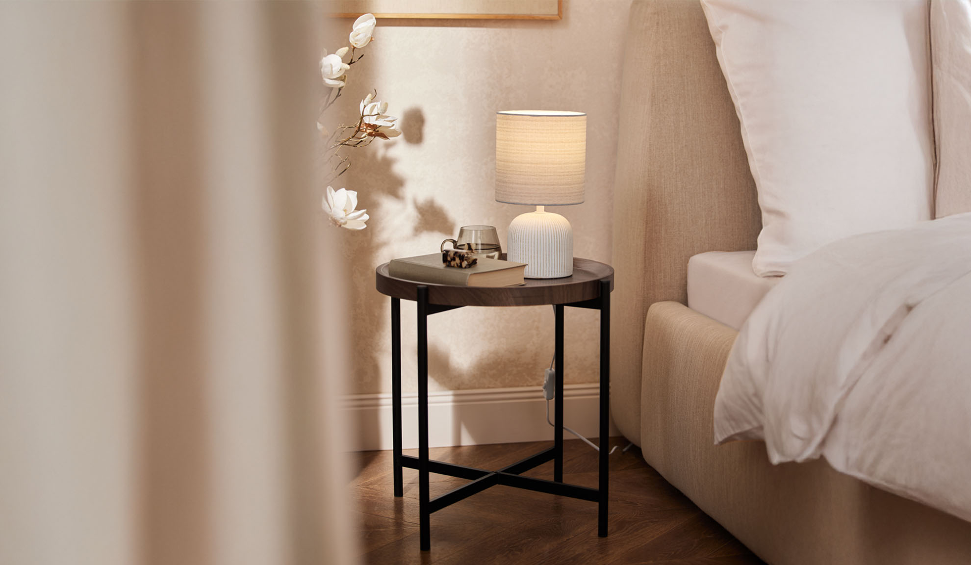 Rundt trænatbord med bordlampe og tilbehør ved siden af en seng.