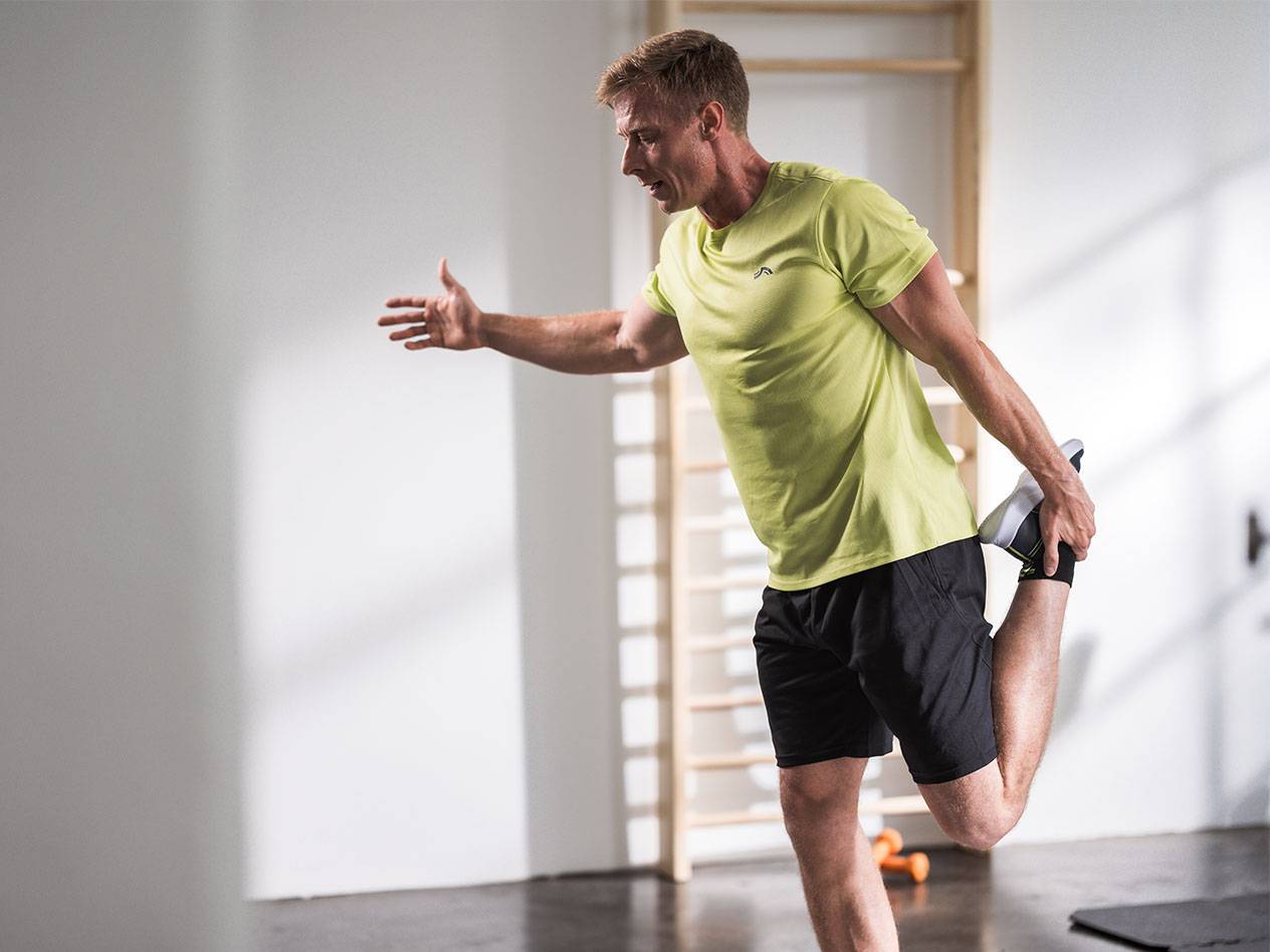 Mand strækker ud i sorte shorts og en limegrøn t-shirt i et fitnesscenter.