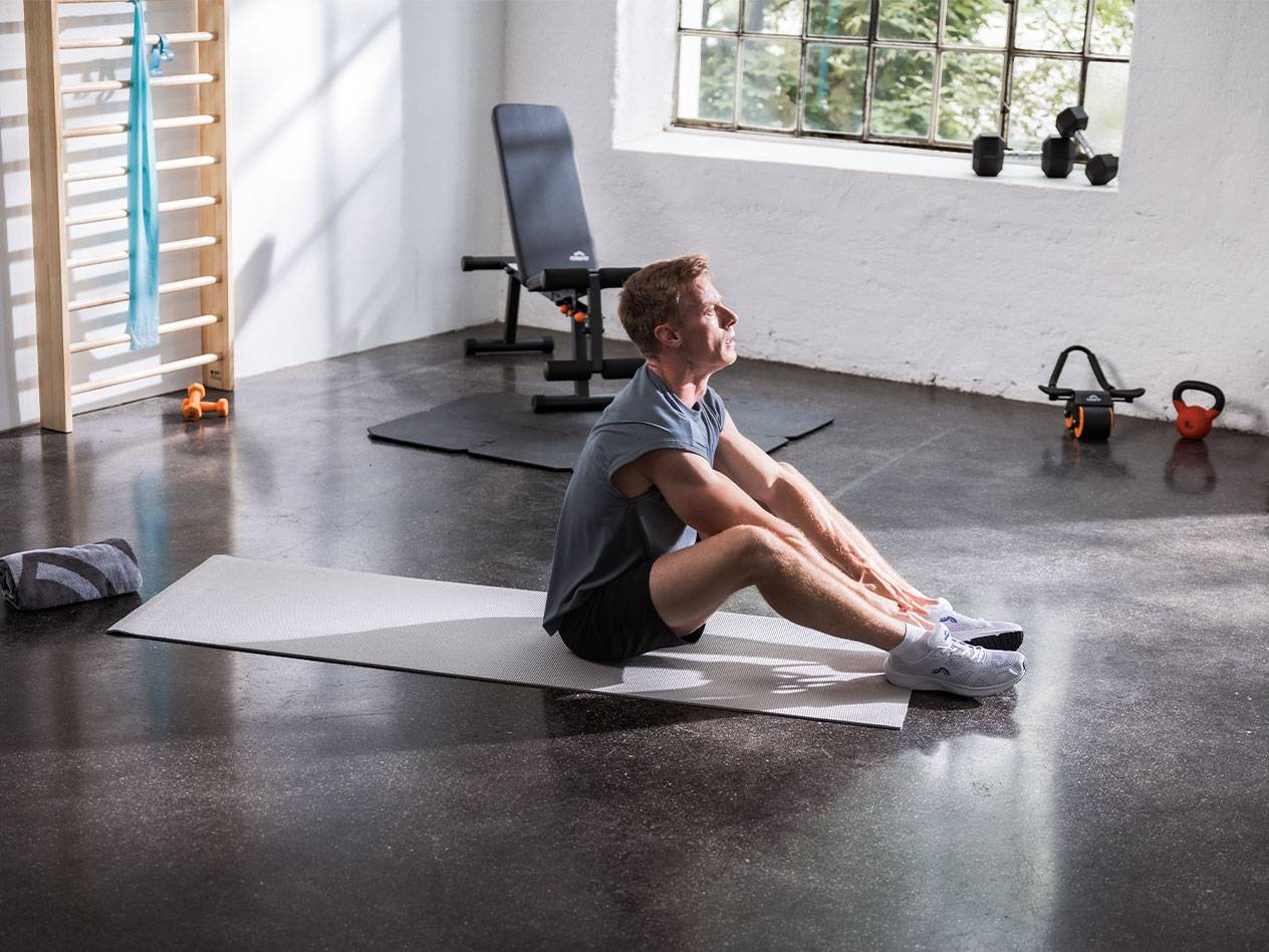 En mand strækker ud på en yogamåtte i et fitnesscenter med udstyr.