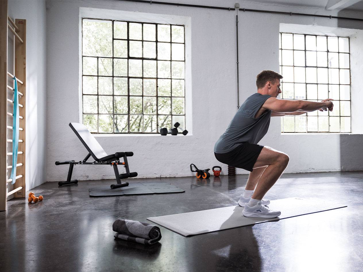 Mand der laver squats i et fitnesscenter med en vægtbænk og måtter.