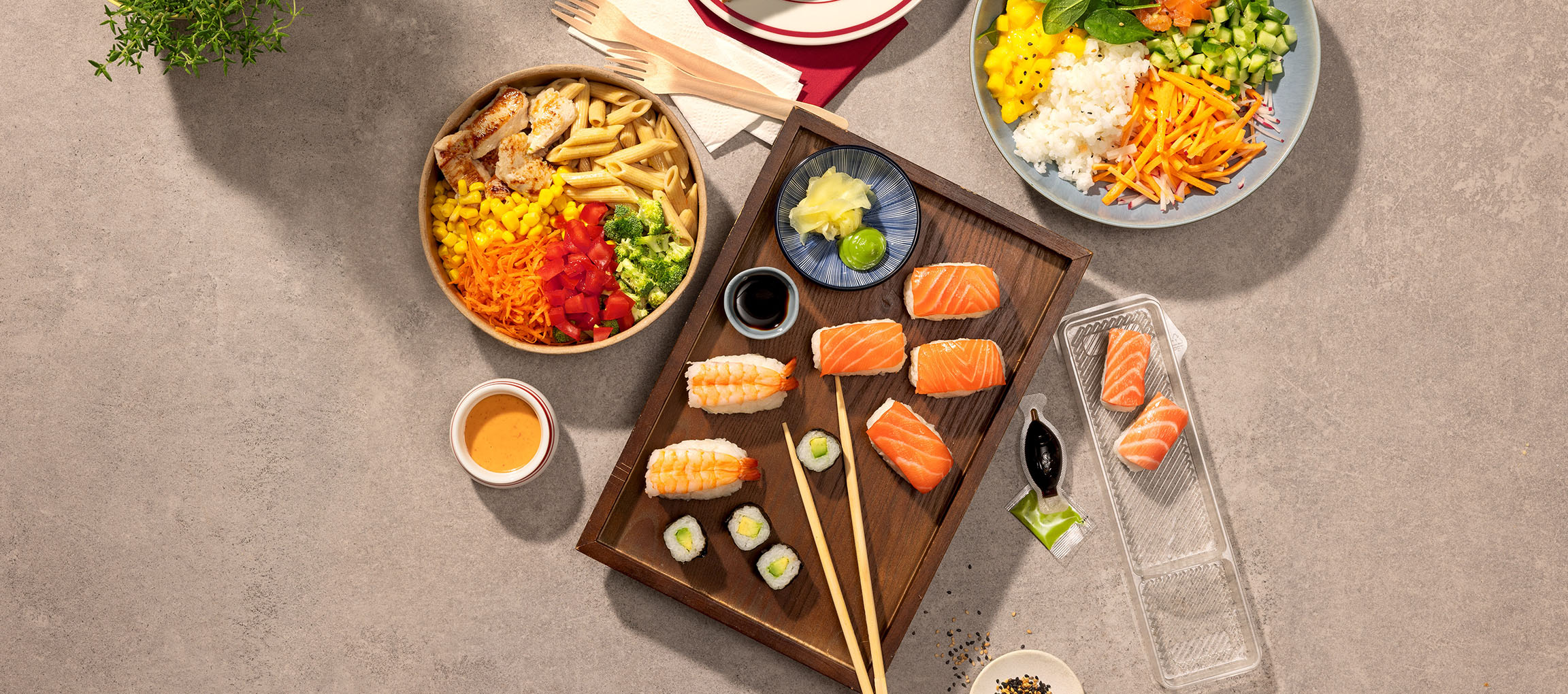 Assorterede retter: pasta- og kyllingeskål, sushi og en poke bowl på et bord.