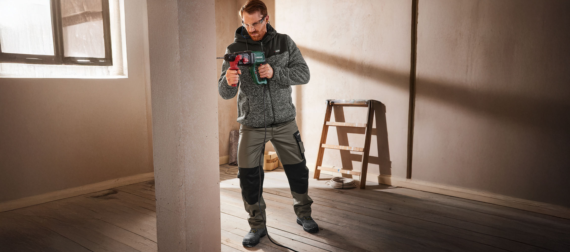 Mand i arbejdstøj borer i væg med boremaskine.