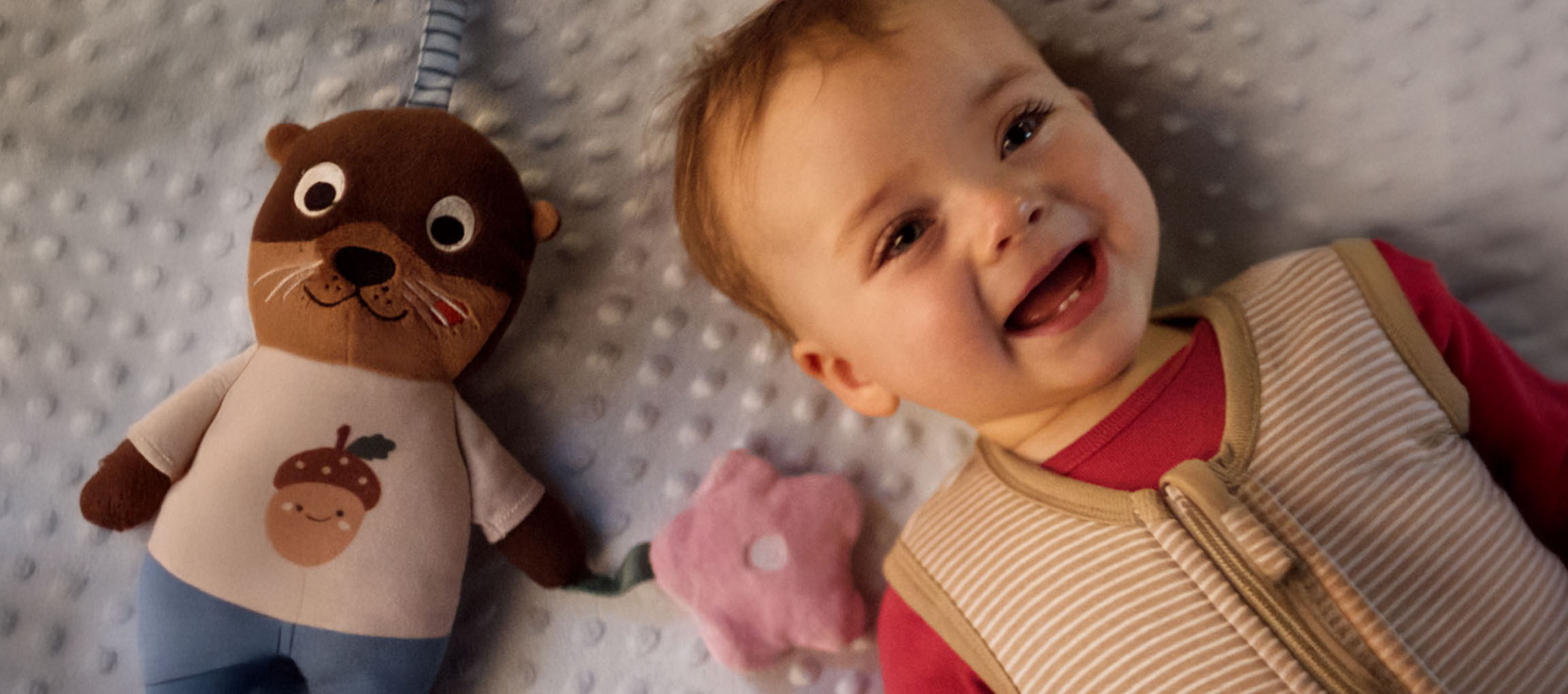 Smilende baby og et plysdyr med et agern på maven.