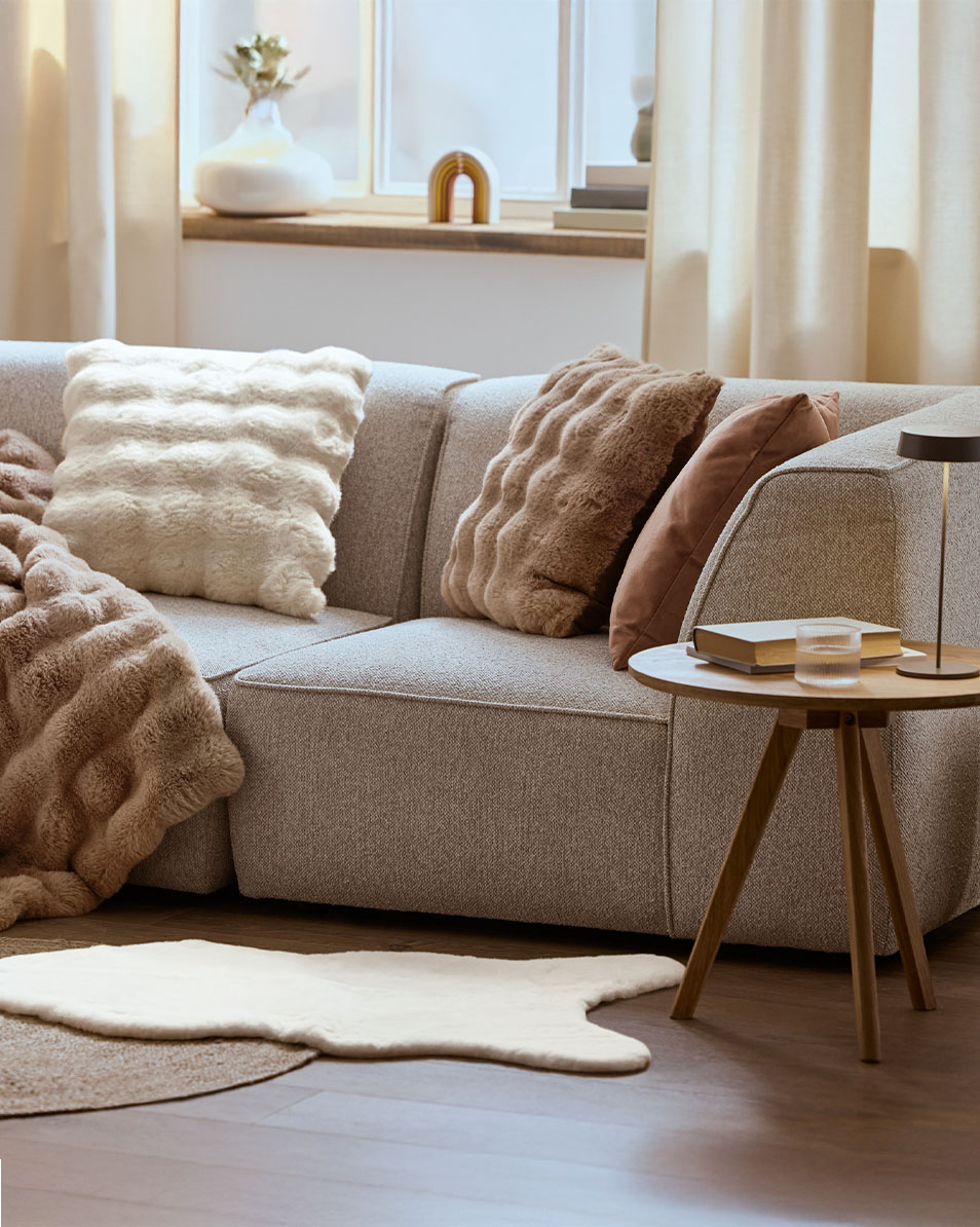 Grå modulsofa med fluffy puder og tæpper, træ sidebord.