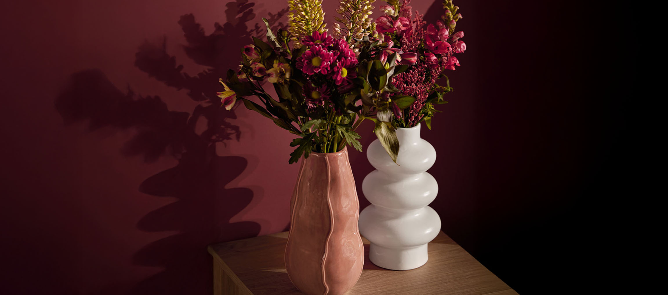 To vaser med blomster, en lyserød og en hvid, på en træoverflade.