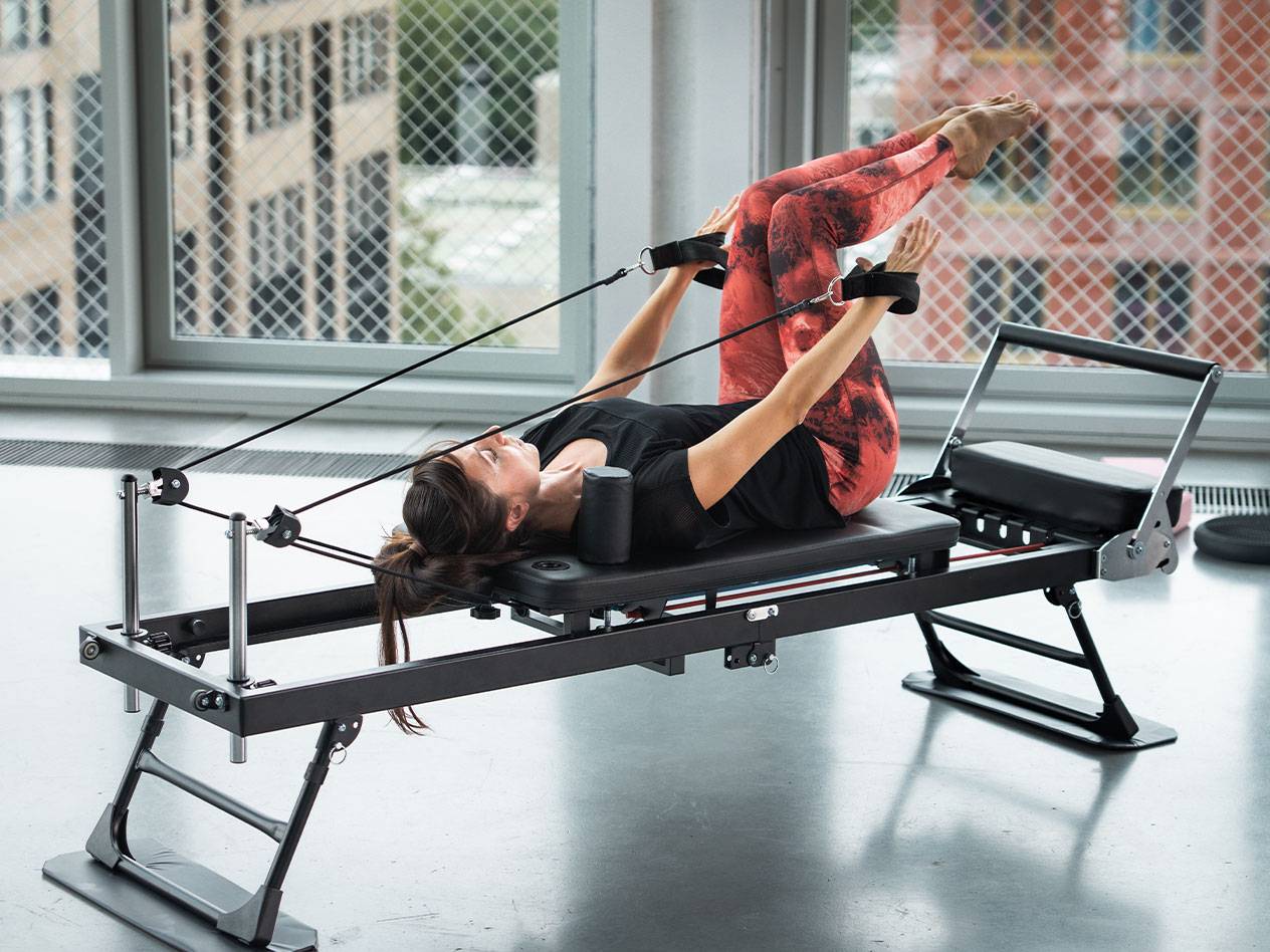 Kvinde træner Pilates på en reformer med røde yogabukser.