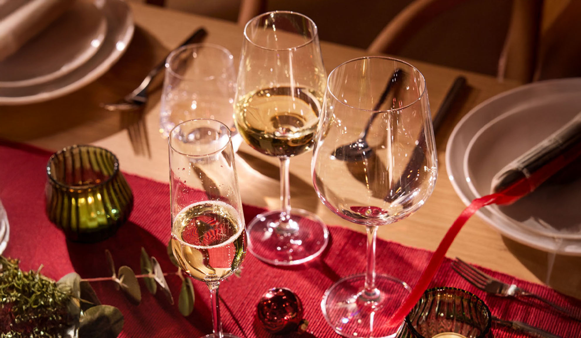 Festligt dækket bord med vinglas, champagneglas og julepynt.