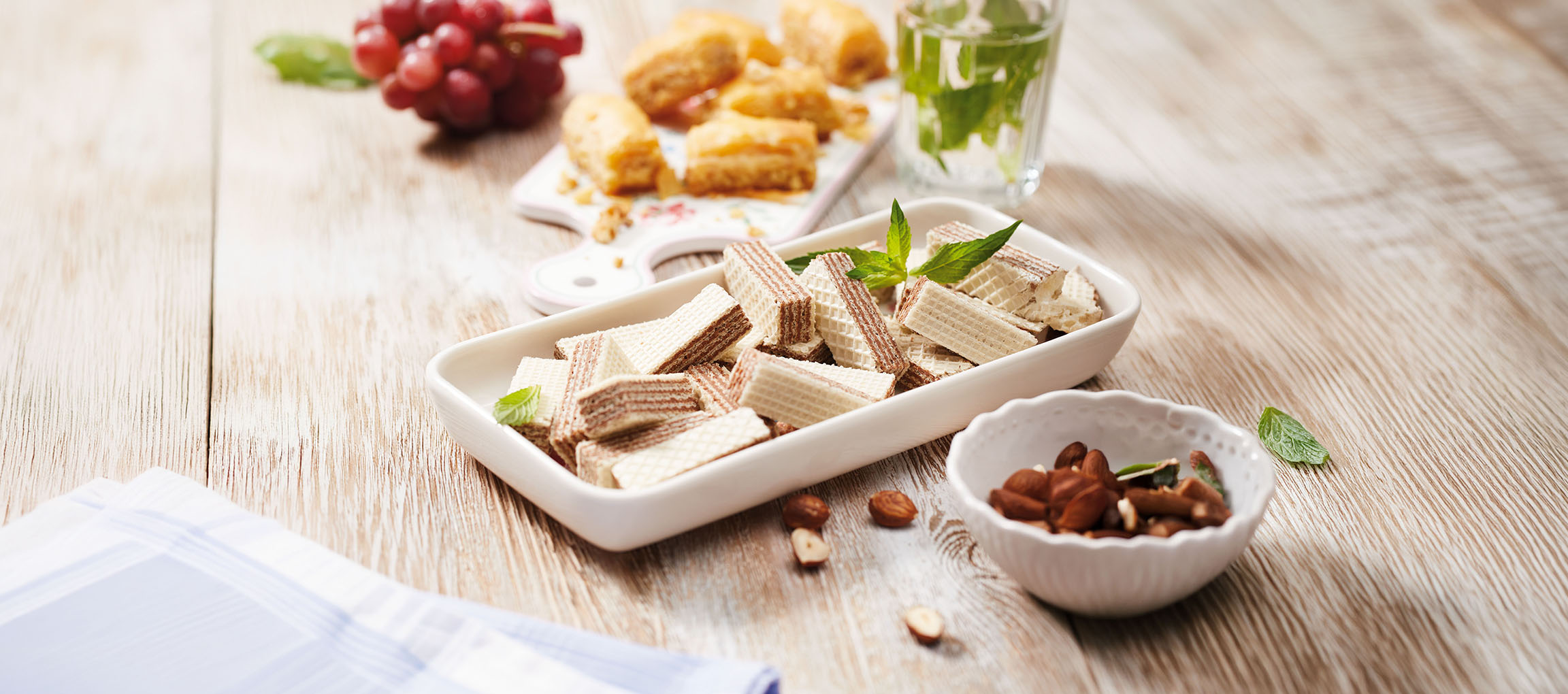 Vafler, baklava, druer og myntevand på et træbord.