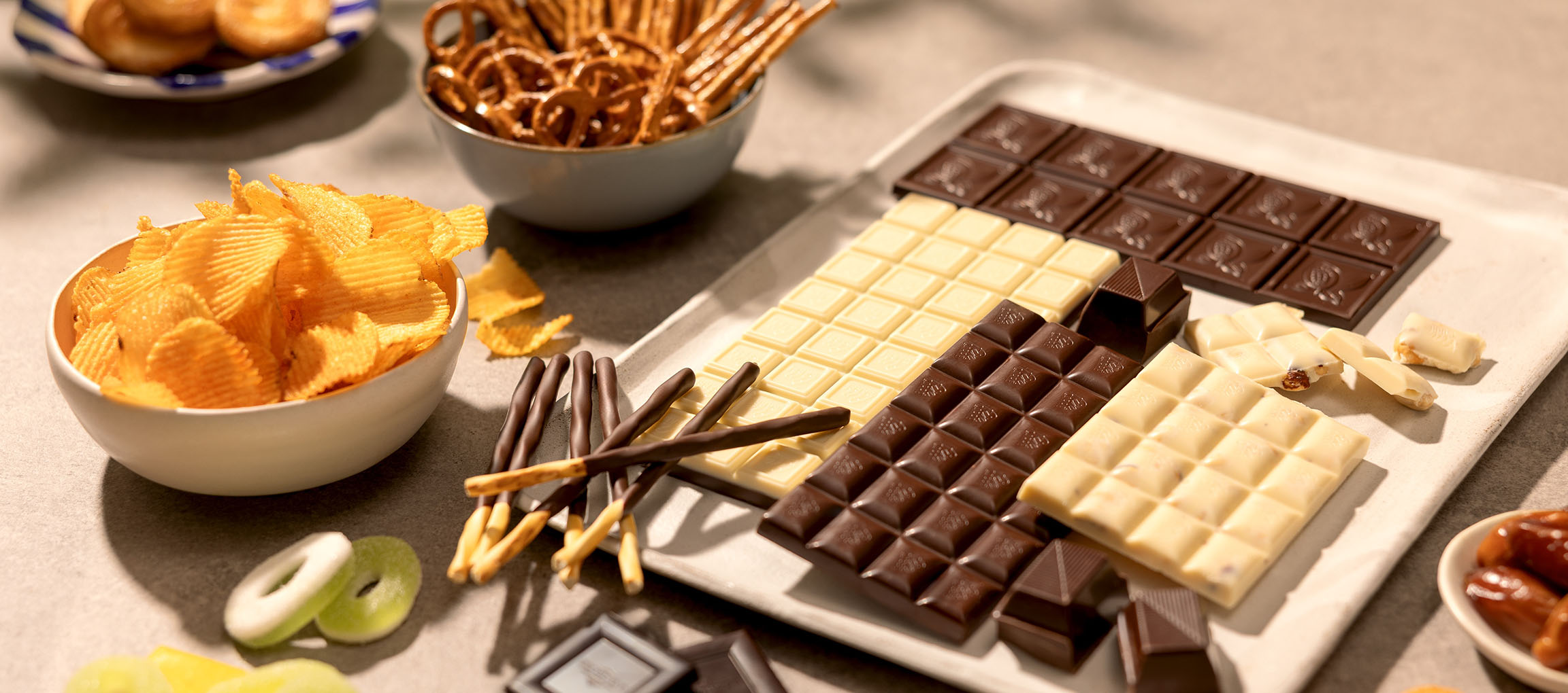 Assorterede chokolader, kartoffelchips, saltkringler og slik på et bord.