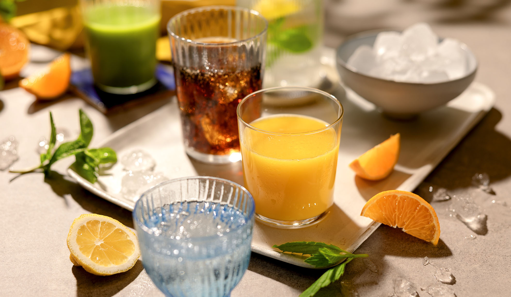 Forskellige forfriskende drikkevarer med is, citrusskiver og mynte på en bakke.