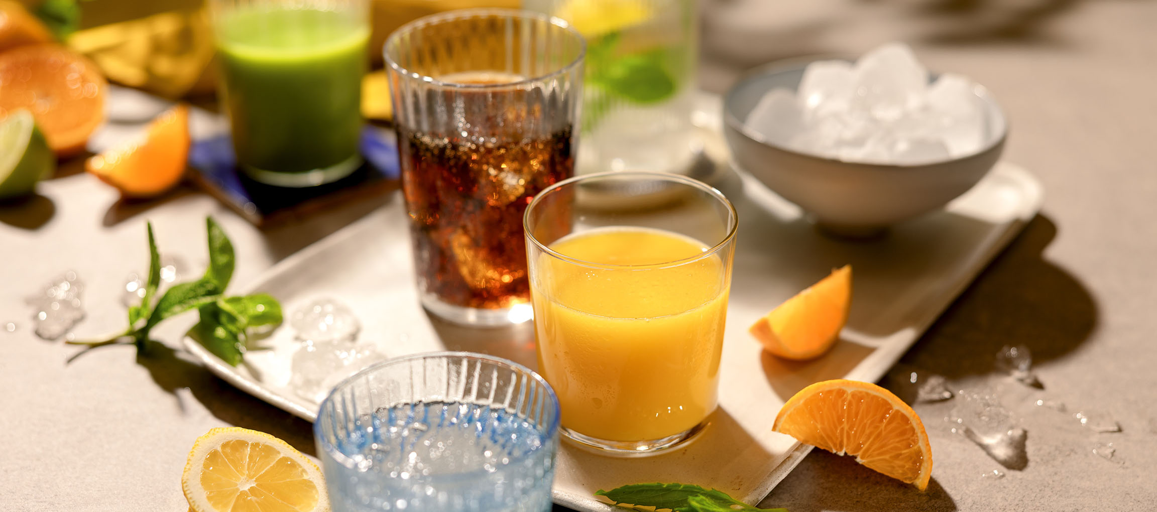 Forskellige forfriskende drikkevarer og frugter på en bakke, herunder appelsinjuice og sodavand.