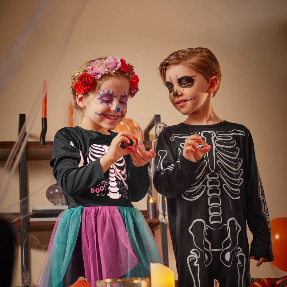 To børn i skeletkostumer med ansigtsmaling, der holder en lille rød genstand.