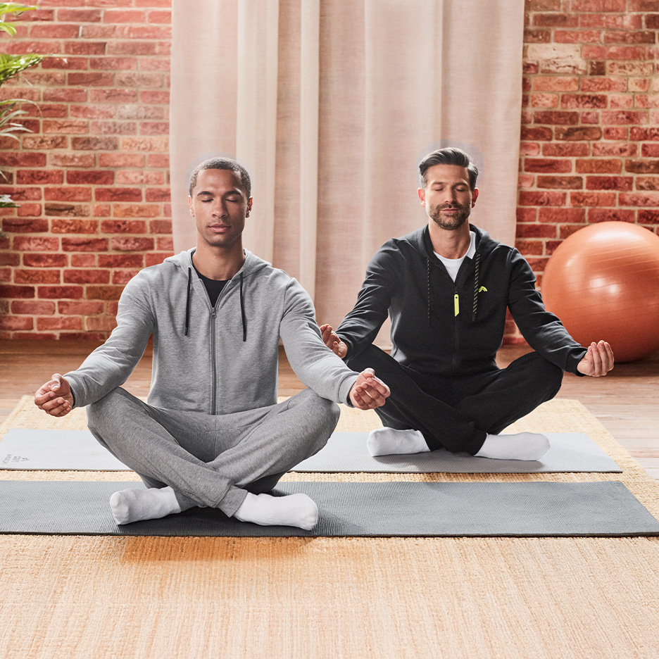 To mænd med lukkede øjne mediterer i matchende træningssæt på yogamåtter.