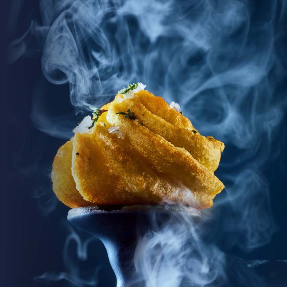 Sprøde, gyldne kartoffelchips med urter og flagesalt på en mørk baggrund med damp.