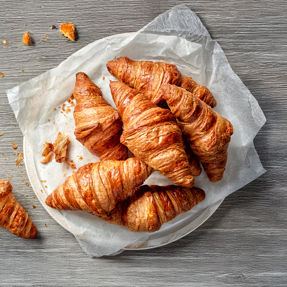 En tallerken med gyldenbrune croissanter på bagepapir på et træbord.