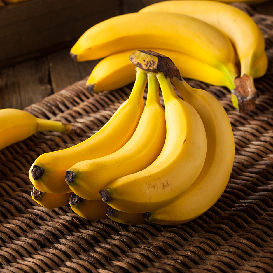 En klynge modne gule bananer ligger på en flettet måtte.