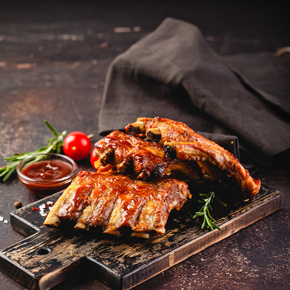 Grillede spareribs med barbecue sauce, rosmarin og tomater på et træskærebræt.
