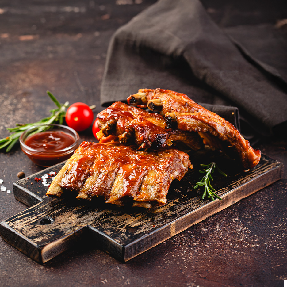 Grillede spareribs med barbecue sauce, rosmarin og cherrytomater på et træskærebræt.
