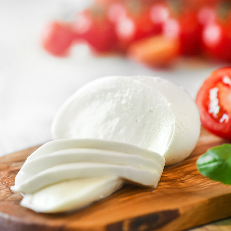 Frisk mozzarella, skåret og hel, med tomater og basilikum på et træbræt.
