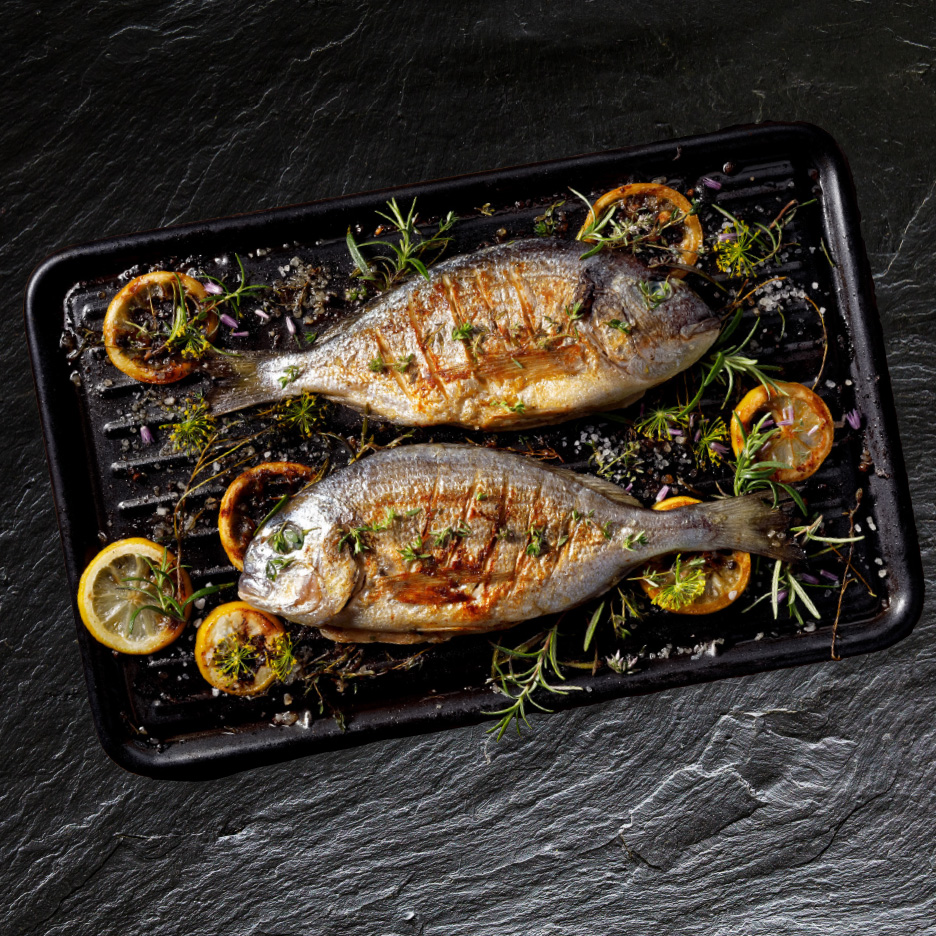 To grillede fisk med citron og krydderurter på en sort grillpande.