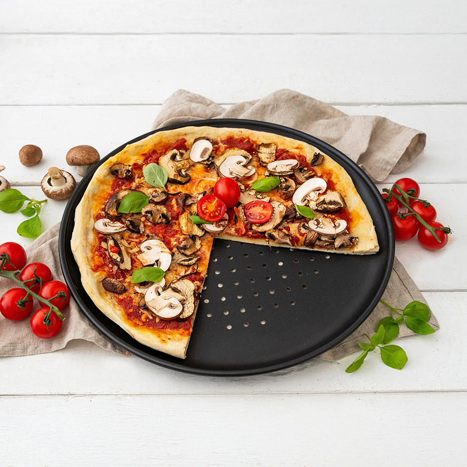 En champignonpizza med tomater og basilikum på en sort bageplade.