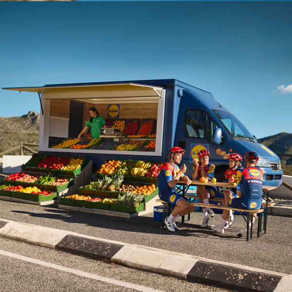 Cyklister holder pause ved en Lidl-lastbil fyldt med frugt og grøntsager.