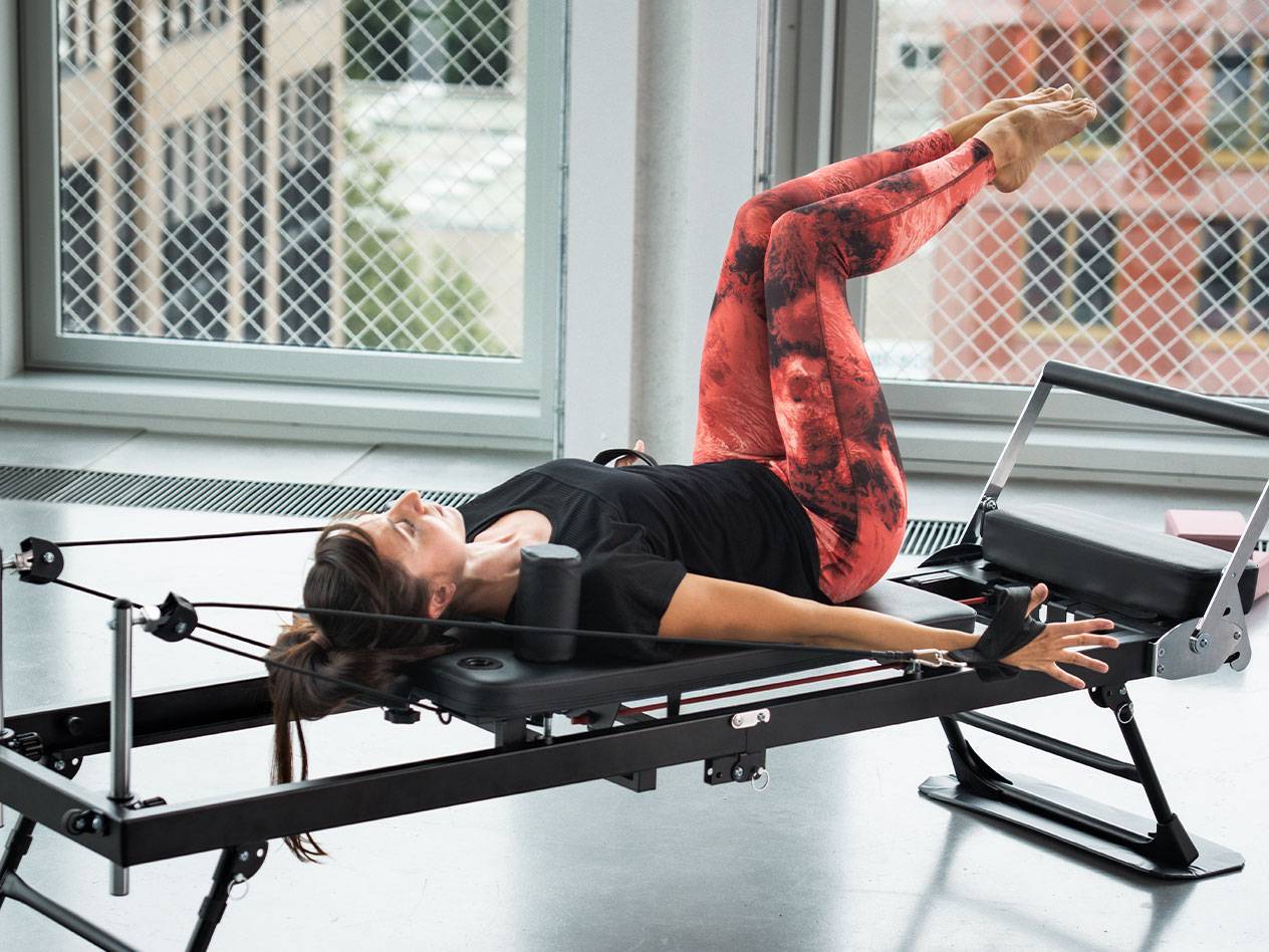 Kvinde laver Pilates på en reformer, i røde og sorte leggings
