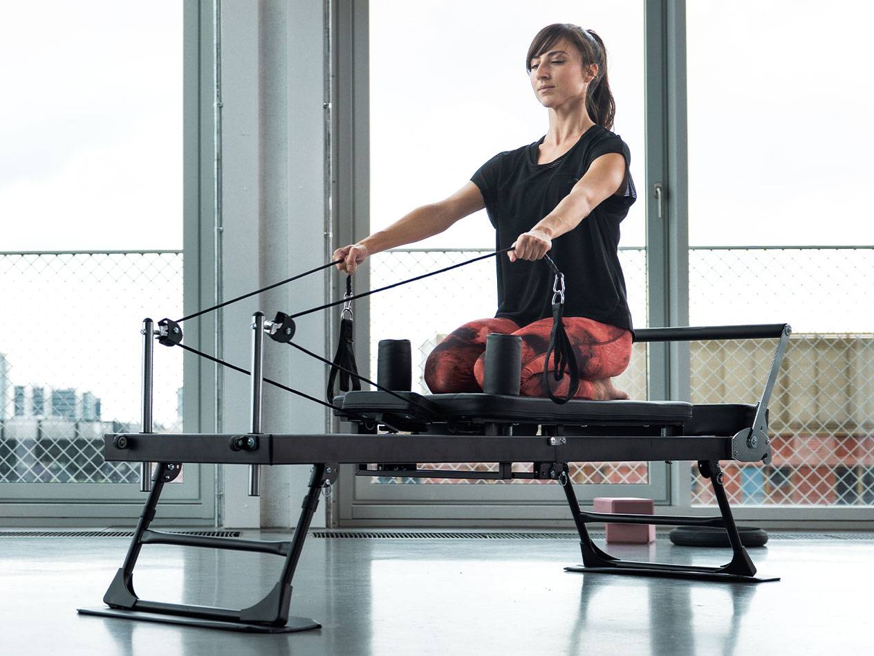 Kvinde laver Pilates på en reformer med store vinduer i baggrunden.