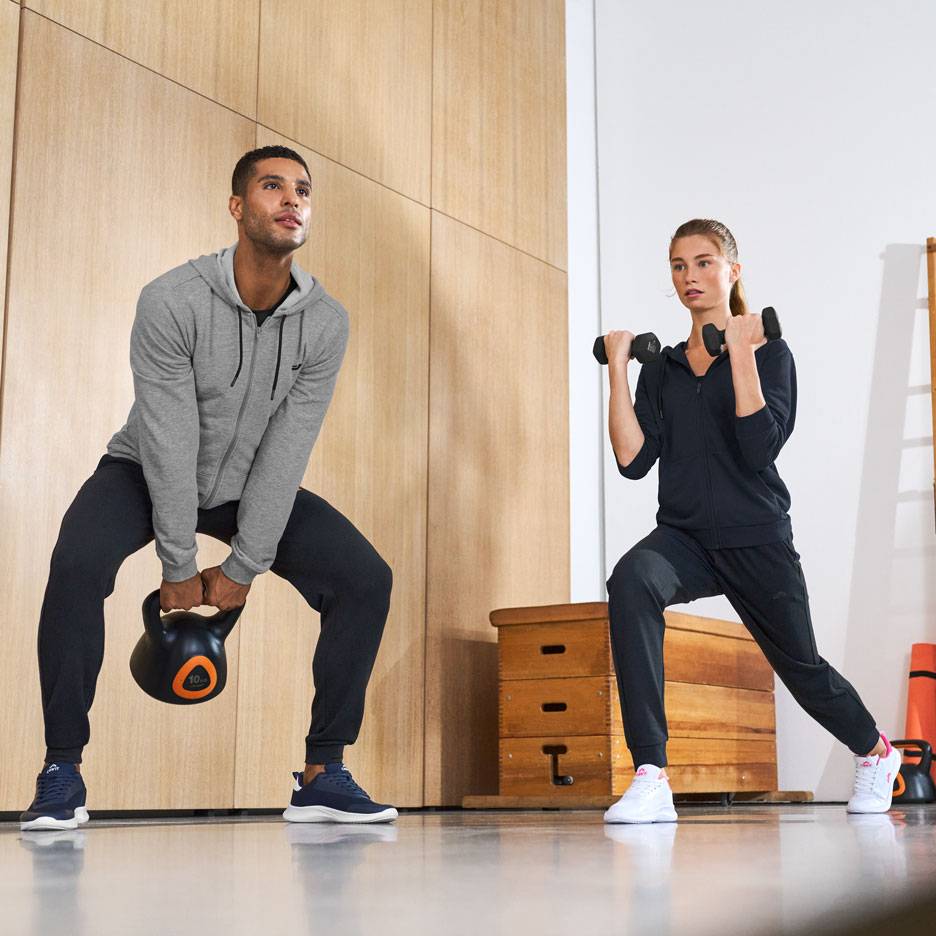 Mand og kvinde i træningstøj, der træner med kettlebell og håndvægte.