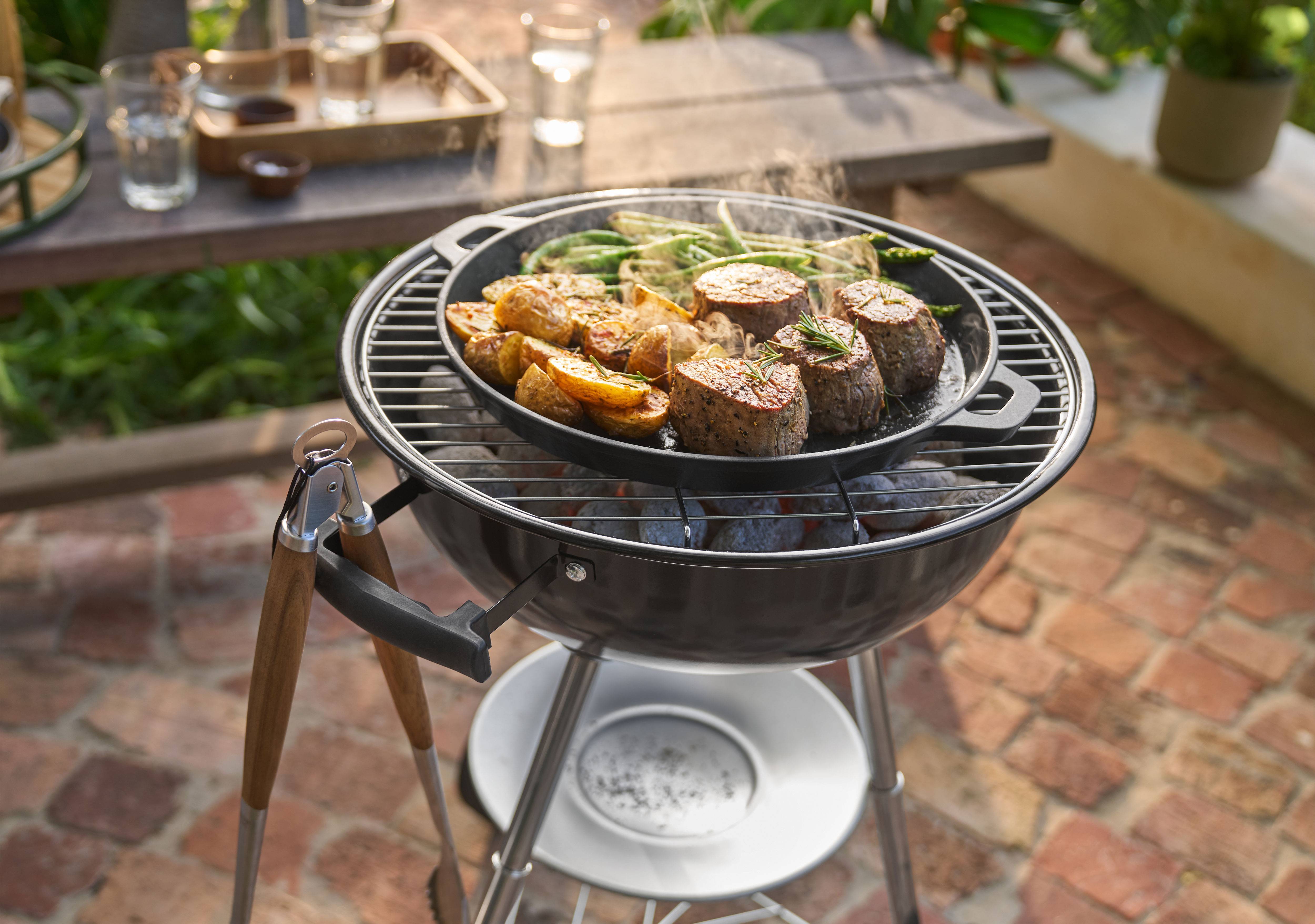 Grill med kød, kartofler og grønne bønner, der tilberedes i en pande udendørs.