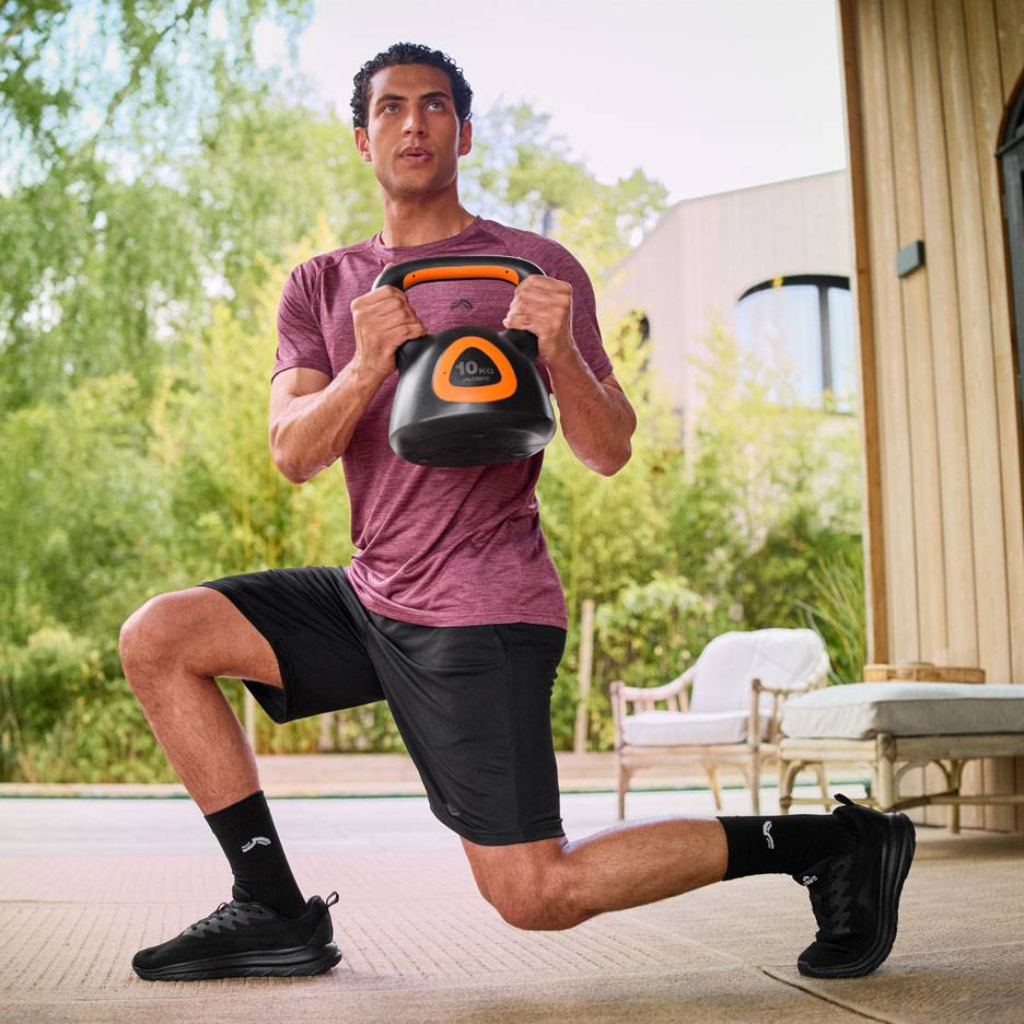 Mand udfører lunges med en 10 kg kettlebell udendørs.