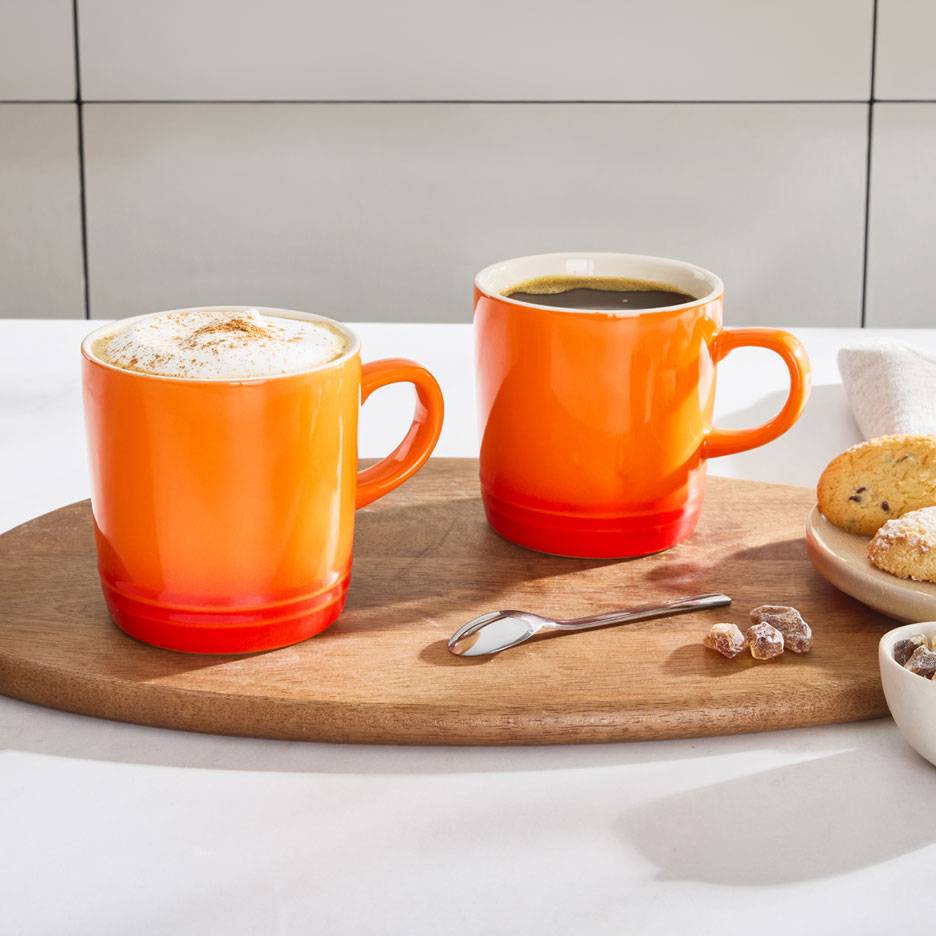 To orange kaffekrus på et træfad, det ene med skumkaffe, det andet med sort kaffe.