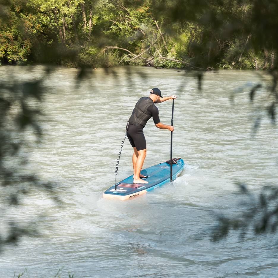 Mand i våddragt og redningsvest padler på et blåt paddleboard på en flod.