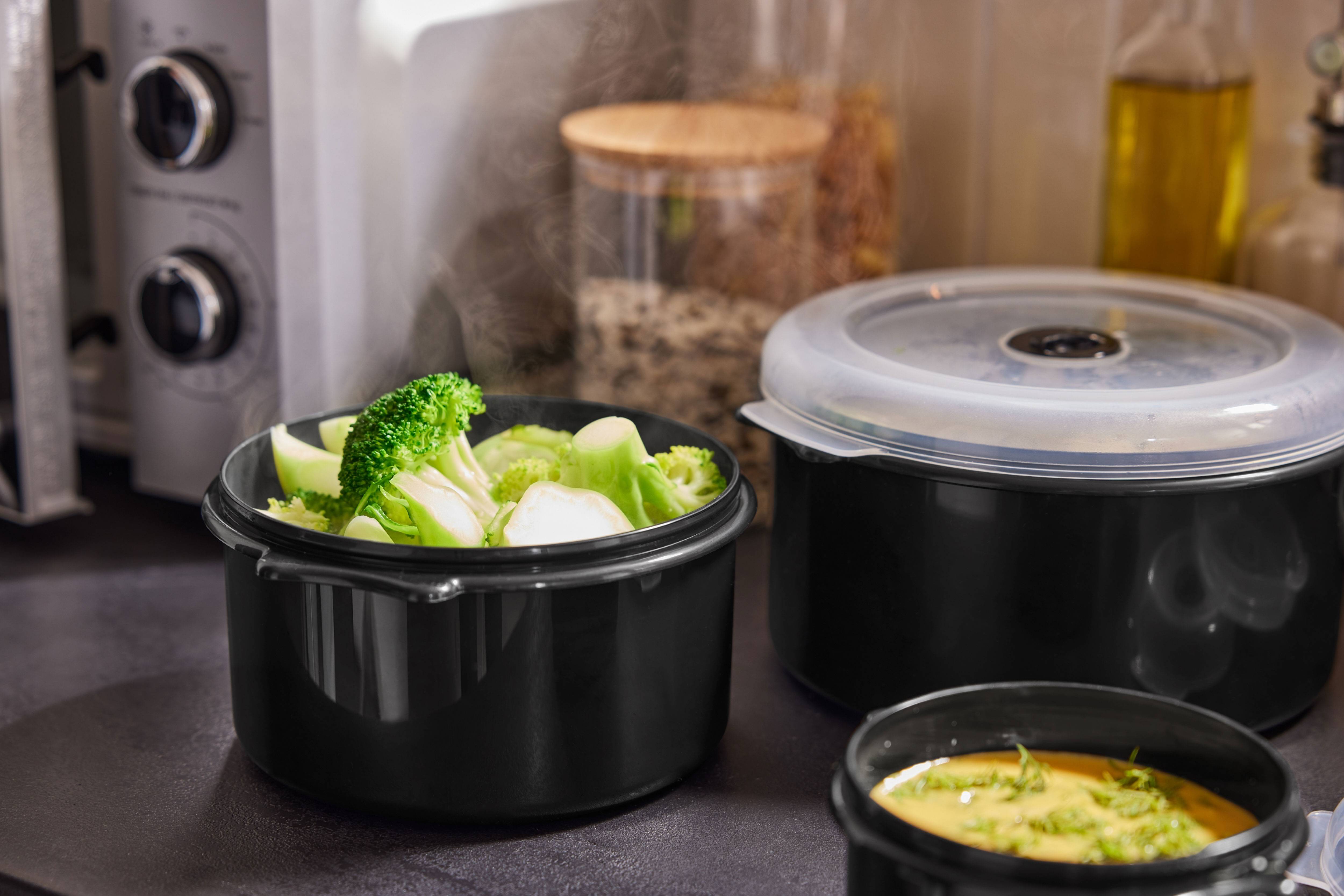 Dampende broccoli og andre retter i sorte beholdere på køkkenbordet.