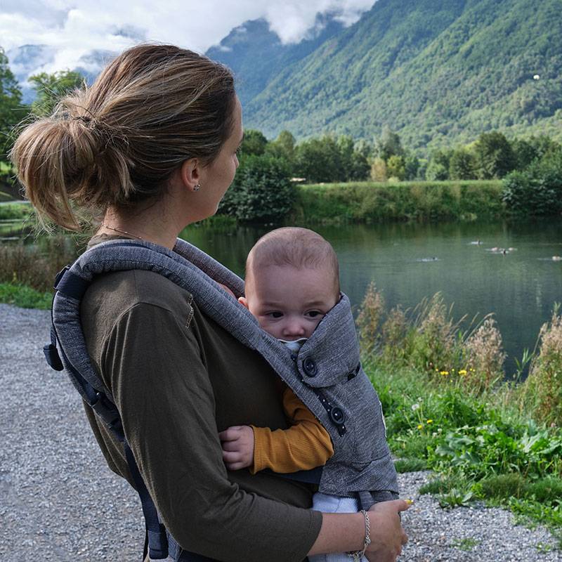 Mor med baby i bæresele ved en sø.
