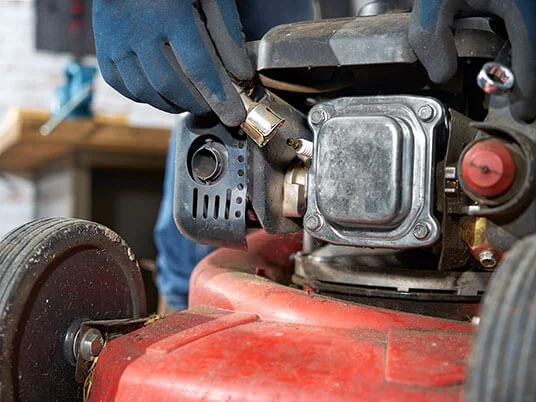 Handsker udskifter tændrøret på en rød plæneklipper.